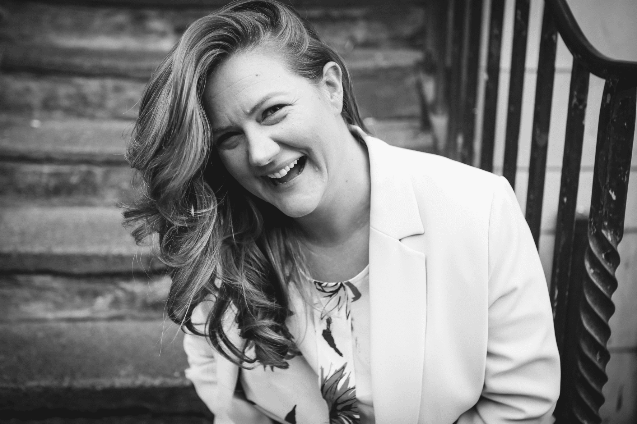 A sweet smile of Alex Worsely wearing a clean pink blazer above her white floral blouse in black and white.